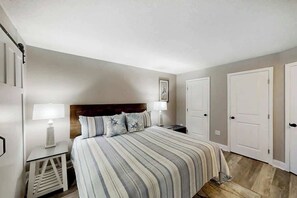 A bedroom with a bed, two bedside tables, a nightstand, and a door. - This is It 2 BR Condo (North Myrtle Beach)