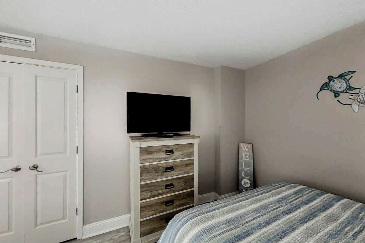 Ein Schlafzimmer mit einem Bett, einem Fernseher auf einer Holzkommode, einem Willkommensschild und einer Wanddekoration.