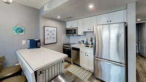 A modern kitchen with stainless steel appliances, white cabinetry, and a small dining area with a bench. - This is It 2 BR Condo (North Myrtle Beach)