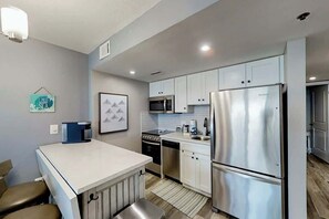 A modern kitchen with stainless steel appliances, white cabinetry, and a small dining area with a bench. - This is It 2 BR Condo (North Myrtle Beach)
