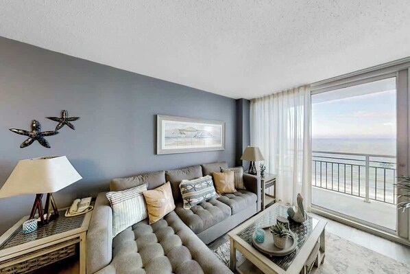 A living room with a sofa, a coffee table, a lamp, and a view of the ocean. - This is It 2 BR Condo (North Myrtle Beach)