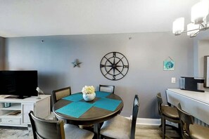 A dining area with a round table, chairs, a wall-mounted compass, and a television. - This is It 2 BR Condo (North Myrtle Beach)