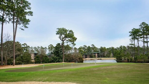 Ein Golfplatz mit Teich, umgeben von Bäumen und Gebäuden.