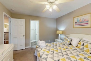 A bedroom with a bed, a nightstand, a ceiling fan, and a door leading to another room.