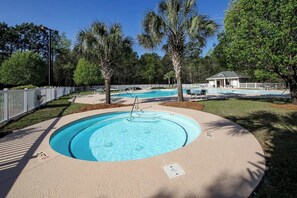 Une piscine circulaire entourée d’une terrasse, de palmiers et d’un espace délimité par une clôture, aménagé avec des chaises longues.