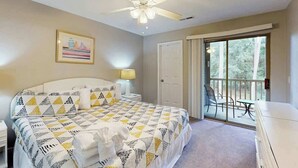 Ein Schlafzimmer mit Bett, Deckenventilator, einer Tür und einem Balkon mit Tisch und Stühlen.