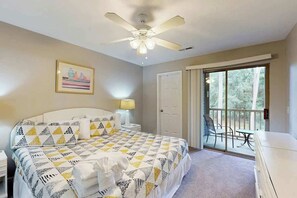 Ein Schlafzimmer mit Bett, Deckenventilator, einer Tür und einem Balkon mit Tisch und Stühlen.