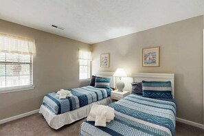 Une chambre d’hôtel avec deux lits, une table de chevet, une lampe et une fenêtre avec des stores.