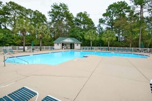 A swimming pool with lounge chairs and a small building, surrounded by trees.