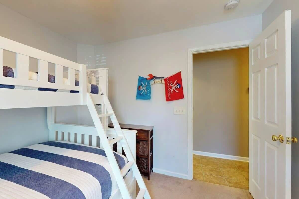 A child's bunk bed with a ladder, a small wooden table, and two flags on the wall.