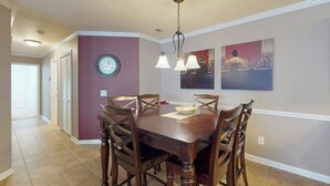 A dining room with a wooden table, six chairs, a clock, and two wall-mounted paintings. - Sterling Pointe 120-A at Wachesaw III (Murrells Inlet)