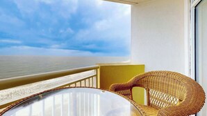 A balcony with a wicker chair and a glass table, overlooking a beach. - Bay Watch Resort 1103 (North Myrtle Beach)