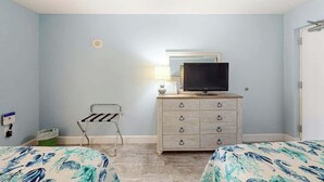 A hotel room with two beds, a dresser with a television, a lamp, and a small chair. - Bay Watch Resort 1103 (North Myrtle Beach)