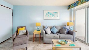 A living room with a grey sofa, a brown armchair, and a wooden coffee table. There are two lamps on side tables, and a framed artwork on the wall. - Bay Watch Resort 1103 (North Myrtle Beach)