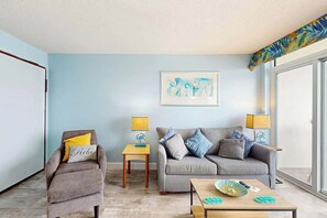 A living room with a grey sofa, a brown armchair, and a wooden coffee table. There are two lamps on side tables, and a framed artwork on the wall. - Bay Watch Resort 1103 (North Myrtle Beach)