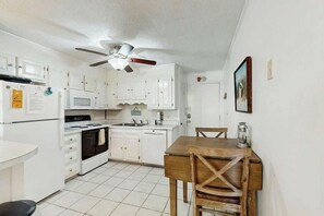 A compact kitchen with white cabinets, a microwave, a stove, and a ceiling fan. - Coastal Tranquility Retreat (North Myrtle Beach)