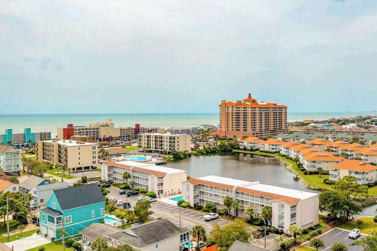 A coastal residential area with a prominent hotel featuring a red roof, surrounded by smaller buildings and a body of water.