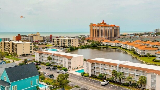 A coastal hotel with multiple buildings, a swimming pool, and a body of water. - Coastal Tranquility Retreat (North Myrtle Beach)