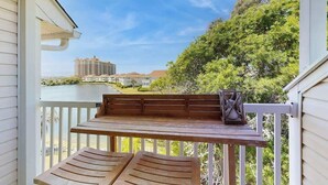 A wooden bench and table on a balcony with a view of a building and trees. - Coastal Tranquility Retreat (North Myrtle Beach)