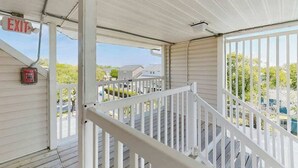 A covered outdoor area with a white railing, an exit sign, and a fire extinguisher. - Coastal Tranquility Retreat (North Myrtle Beach)