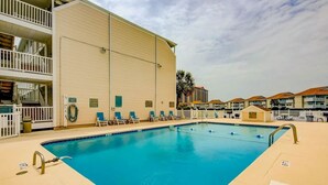 A swimming pool with lounge chairs, a multi-story building with balconies, and a clear sky. - Coastal Tranquility Retreat (North Myrtle Beach)