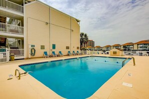 A swimming pool with lounge chairs, a multi-story building with balconies, and a clear sky. - Coastal Tranquility Retreat (North Myrtle Beach)