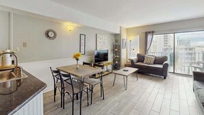 En modern lägenhet med ett matområde, en soffa, en TV och en balkong med utsikt över staden.