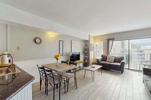 Eine moderne Wohnung mit Essbereich, einer Couch, einem Fernseher und einem Balkon mit Stadtblick.