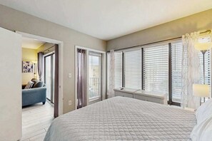 Ein Schlafzimmer mit einem großen Bett, einem Fenster mit Jalousien, einem Heizkörper und einem Sofa im angrenzenden Raum.