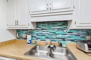 A kitchen with white cabinets, a stainless steel sink, and a tiled backsplash. - Shipwatch Pointe II P-105 (Myrtle Beach)