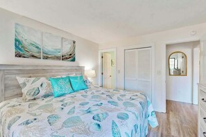 A bedroom with a bed, a nightstand, a mirror, and a door leading to another room. - Shipwatch Pointe II P-105 (Myrtle Beach)