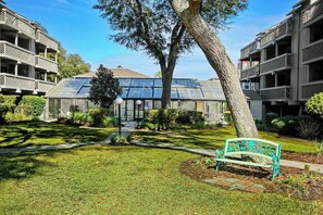 Un patio con un banco, un edificio con techo de vidrio y un árbol.