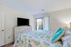 A bedroom with a bed, a TV on a dresser, and a sliding glass door to the outside. - Shipwatch Pointe II P-105 (Myrtle Beach)
