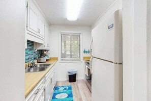 A compact kitchen with white cabinets, a stainless steel sink, and a window with blinds. - Shipwatch Pointe II P-105 (Myrtle Beach)