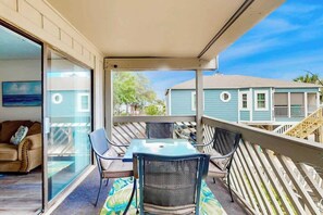 A covered outdoor seating area with a table and chairs, a sliding glass door leading to an interior room, and a view of neighboring houses. - Shipwatch Pointe II P-105 (Myrtle Beach)