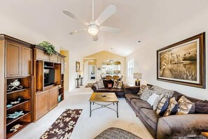 A spacious living room with a ceiling fan, a large painting, and a sofa with multiple cushions. - River Crossing Unit 131 (North Myrtle Beach)