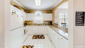 A kitchen with white cabinets, a granite countertop, and a window with blinds. - River Crossing Unit 131 (North Myrtle Beach)