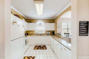 A kitchen with white cabinets, a granite countertop, and a window with blinds. - River Crossing Unit 131 (North Myrtle Beach)