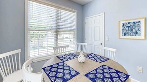 A dining area with a round table, white chairs, and blue patterned placemats. - Surfside Escape Retreat (Surfside Beach)