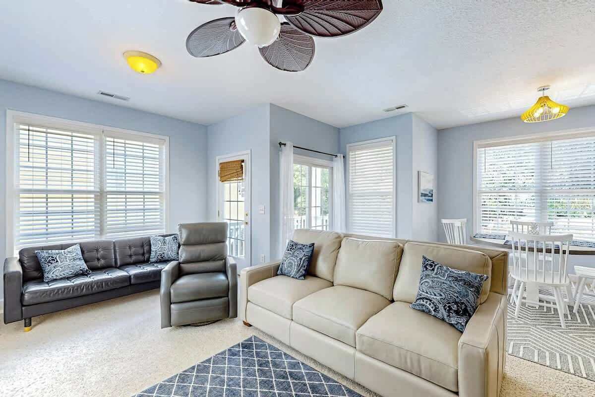 A living room with a sofa set, a chair, a ceiling fan, and a dining area with white chairs.