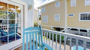 A wooden deck with a blue chair, a white railing, and a yellow building in the background. - Surfside Escape Retreat (Surfside Beach)