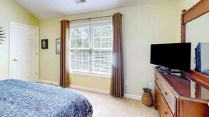 A bedroom with a bed, a dresser, a television, and a window with curtains. - Surfside Escape Retreat (Surfside Beach)