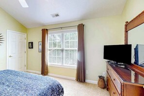 Ein Schlafzimmer mit einem Bett, einer Kommode, einem Fernseher und einem Fenster mit Vorhängen.