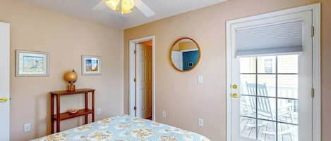 A bedroom with a bed, a ceiling fan, a door with a view to the outside, and a small table with a globe.