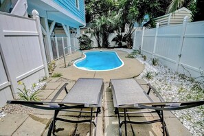Ein Garten mit Swimmingpool, zwei Liegestühlen, einem weißen Zaun und einem blauen Haus.