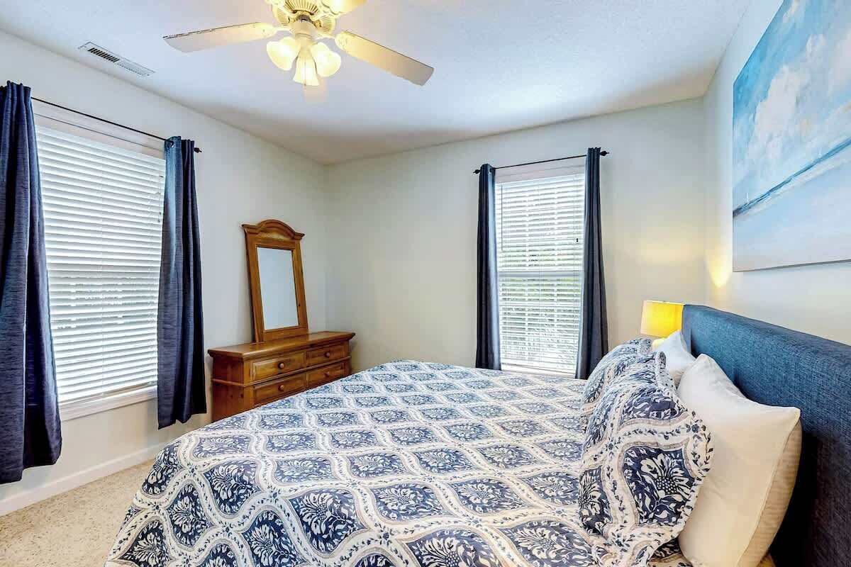 Une chambre à coucher avec un lit, une commode, un ventilateur de plafond et un tableau accroché au mur.