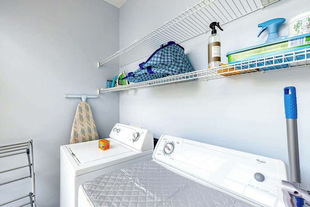 A laundry room with two dryers, a rack, and shelves with cleaning supplies.