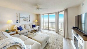 A hotel room with a balcony, a flat-screen TV, a sofa, a coffee table, and a ceiling fan. - Endless Summer Oasis (North Myrtle Beach)