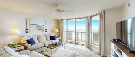 A hotel room with a balcony, a flat-screen TV, a sofa, a coffee table, and a ceiling fan.