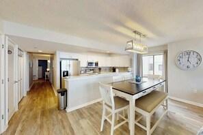 A modern kitchen with white cabinetry, a central island, and a dining area with a table and chairs. - Endless Summer Oasis (North Myrtle Beach)